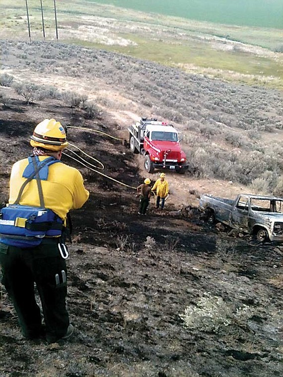 Grant County Fire District No. 10 firefighter Lynn Lindsey, with back to camera, firefighter Tim Freeman, facing camera, and another firefighter work a wild land fire that was ignited by a burning pickup.