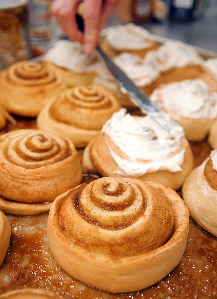 Monique Foster spreads cream topping over freshly baked Cinnamon Rolls on Thursday morning at Bad Dog Bakery in Kalispell.