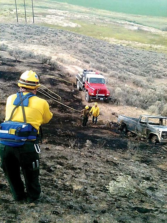 Grant County Fire District No. 10 firefighter Lynn Lindsey, with back to camera, firefighter Tim Freeman, facing camera, and another firefighter work a wild land fire that was ignited by a burning pickup.