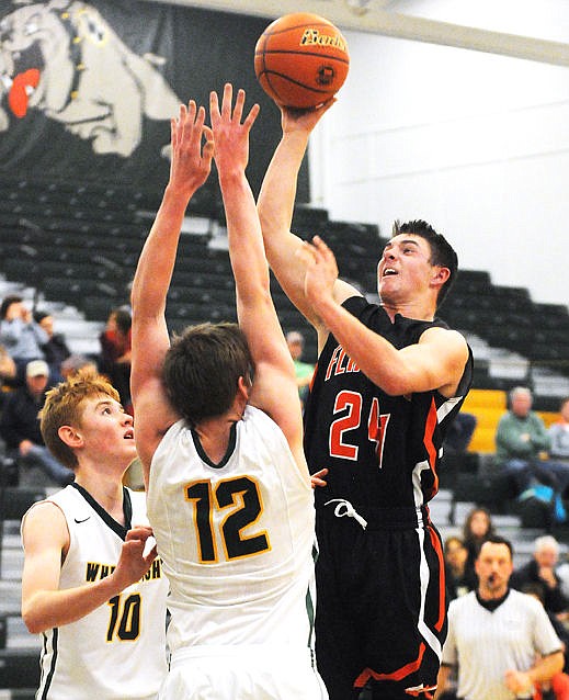 <p>Flathead's C.J. Dugan sinks a basket over the Bulldogs' Matt Brewer (12) and Jacob Henry (10) to give Flathead an 18-13 lead at halftime in Whitefish on Tuesday. (Aaric Bryan/Daily Inter Lake)</p>