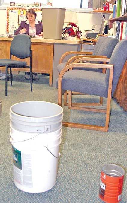 Brandon Roberts/The Western News Asa Wood Elementary principal Margie O'Brien-Johnson works around a garbage can doubling as a water pail to catch leaks above her desk. Winter weather has had students and staff at Libby schools dodging puddles and pails in recent weeks.