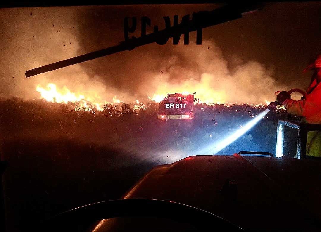 Gonzalez pours water from a cage at the front of a truck at a nighttime wildfire.