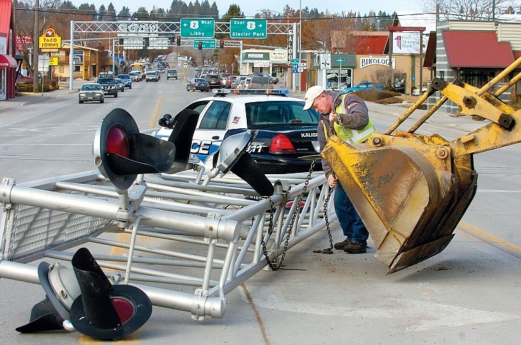 Matt Guckenberg chains a fallen railroad-crossing light tower for removal Thursday afternoon in downtown Kalispell. A truck carrying a piece of logging machinery traveling south on Main Street, with a total height of 16 feet, 4 inches, struck the light tower and knocked it into the turn lane. &#147;I&#146;m glad no one got hurt,&#148; Kalispell Police officer Stan Ottosen said. The accident is under investigation.