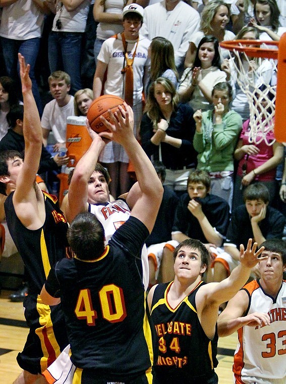 Flathead's Jeremy Grosswiler hangs up in the air before getting off a shot while Missoula Hellgate's Jesse Ginn (40) and Sam Hall (left) defend in the third quarter of Thursday evening's Western AA basketball playoff game at Flathead High School.