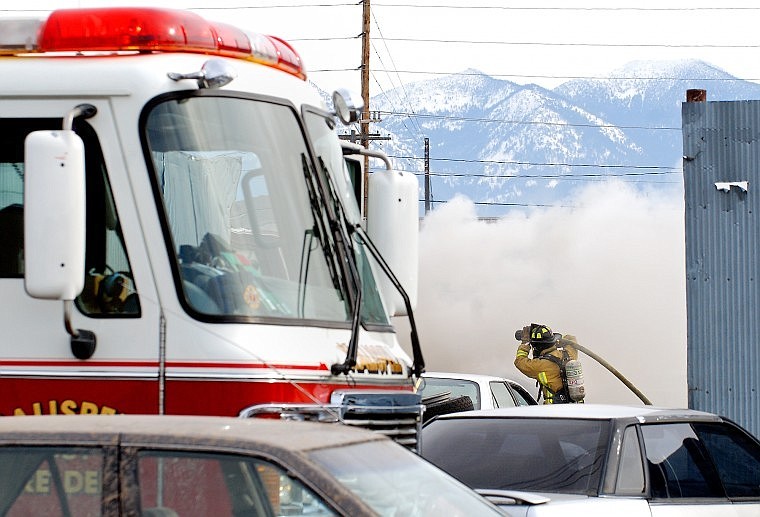 A Kalispell firefighter pulls in a hose as smoke rises at Kalispell Wrecking on Wednesday morning. A worker was using a torch that ignited a trash pile.