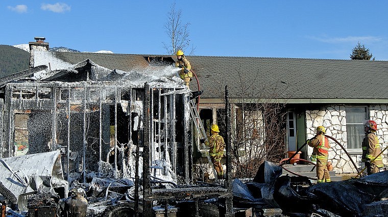 Creston firefighter Tracy Wildes-Mayhood sprays down the garage from the roof of a home near Creston Sunday afternoon. Creston, Bad Rock and Evergreen firefighters responded to a garage fire at 2 p.m. Sunday that spread to part of a home at 405 Cayuse Lane. Three people were treated for minor injuries and smoke inhalation; all were released by Sunday evening. A dog and cat died in the fire.