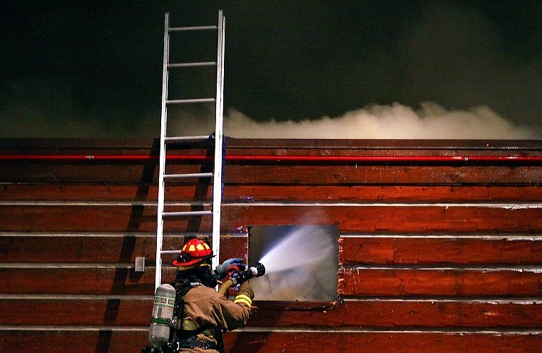 Evergreen Firefighter Ryan Pitts sprays water into the side of the building as smoke rises above.