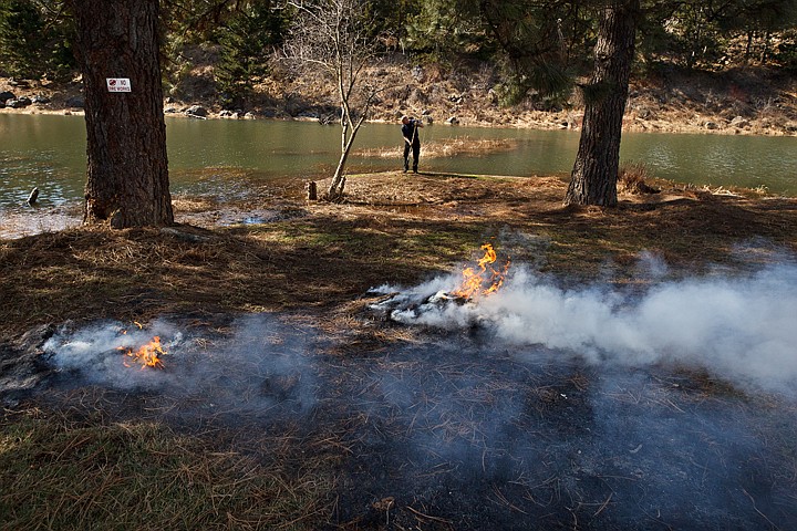 &lt;p&gt;SHAWN GUST/Press Kelly Leatham, a parks maintenance worker for Kootenai County, rakes pine needles as a pair of slash piles burn Thursday near Fernan Lake.&lt;/p&gt;