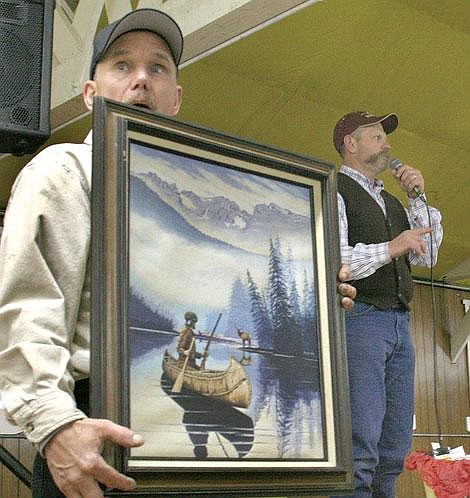 Photo by Adam Herrenbruck Frank Saafeld shows off a Raymond Morgan painting while auctioneer Jeff Jedlicka calls for bidders at the Soul Savers Association Sportsman&#146;s Banquet Saturday at the Sanders County fairground pavilion in Plains.