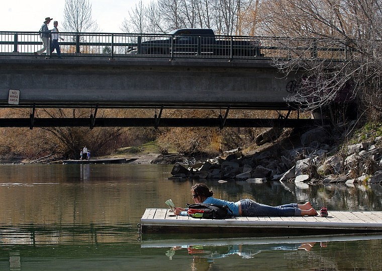 Sarah Hafen reads a book on a dock on the Whitefish River next to the Baker Avenue bridge in Whitefish Friday afternoon. The Montana Department of Transportation is considering plans to rebuild U.S. 93 through downtown Whitefish and convert Baker Avenue into a truck route. One plan calls for widening the bridge.