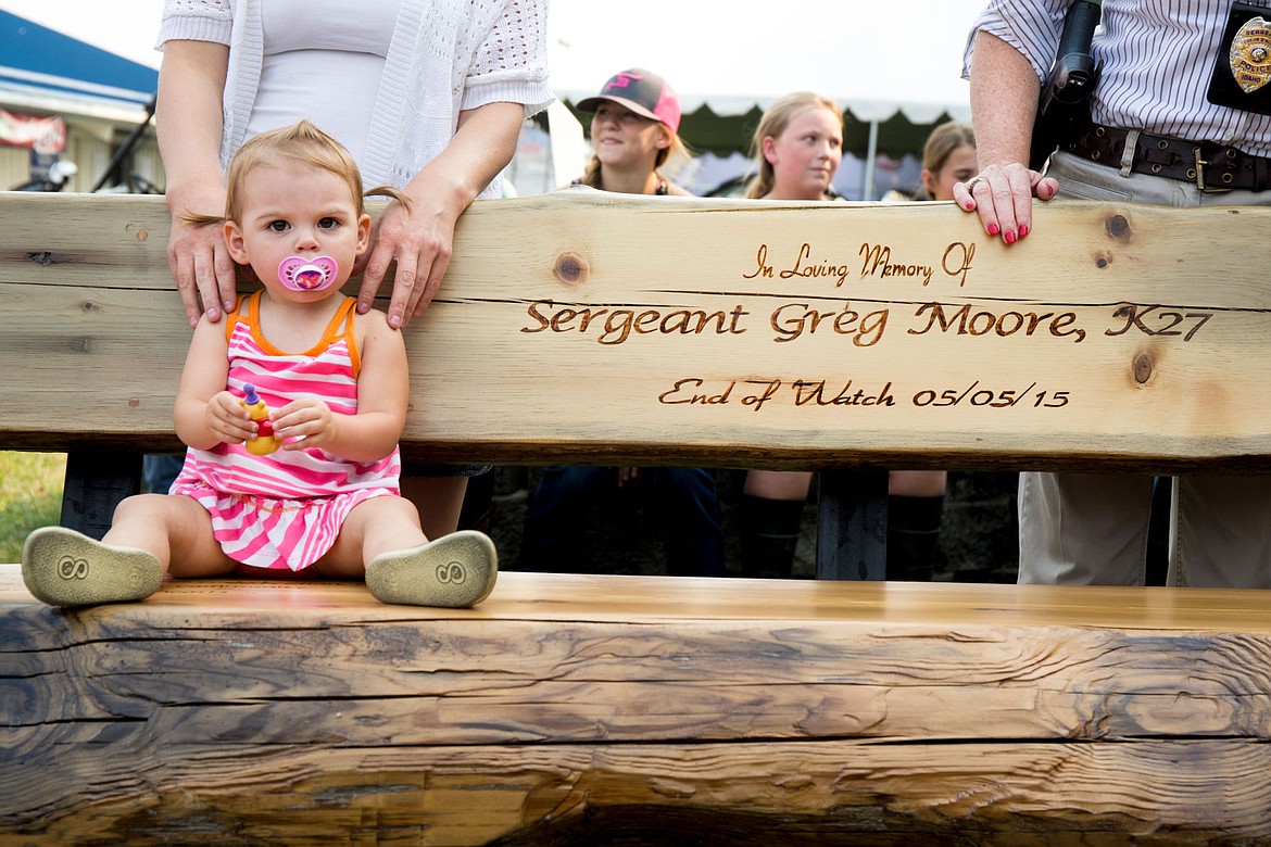 &lt;p&gt;With her mother Lindy&#146;s hands on her shoulders, Jemma Moore, 1, sits on a wooden bench dedicated of her father, Coeur d&#146;Alene Police Sgt. Greg Moore, at an unveiling ceremony for the bench Tuesday, Aug. 25, 2015 at the Kootenai County Fairgrounds. Wild Western Rustic Home Furnishings and children in 4-H Club created the bench in honor of the fallen police officer. The bench will be on display during the North Idaho Fair this weekend.&lt;/p&gt;