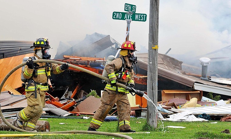 Two Columbia Falls firefighters carry a hose around what is left of the home. Residents throughout the town say they heard and felt the explosion.