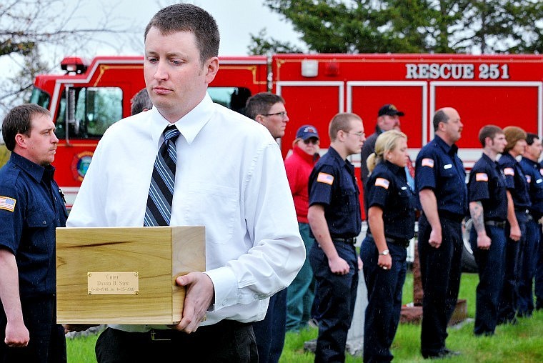 D.J. Sipe, son of former Whitefish Fire Chief David Sipe, carries his father's ashes past a lineup of Whitefish firefighters at Conrad Cemetery in Kalispell Saturday afternoon.