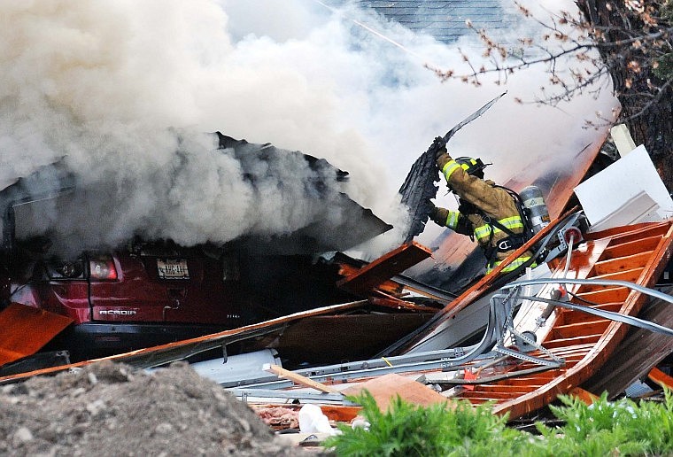 A Columbia Falls firefighter moves a piece of a debris out of the way as smoke rises from a collapsed carport in Columbia Falls Thursday afternoon. A house at 1206 Second Ave. W. exploded around 3:50 p.m., killing a Northwestern Energy employee working about 20 feet away from the building.