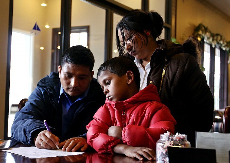 Deepak and Kamala look on as Bal Monger signs paperwork at Flathead Bank in Lakeside on their first full day in the Flathead Valley in mid-April.