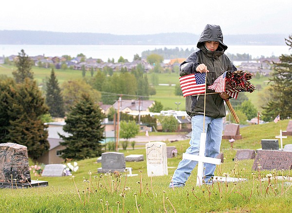 Thirteen-year-old Spencer Raymond helps his boy scout troop and members of the American Legion place crosses and flags on the tombstones of military veterans at the Lakeview Cemetery Saturday morning. Not even a steady rain could deter the men, both young and old from completing their task. &quot;It's something that helps the community,&quot; Raymond said. &quot;It's really good to do for the people who served for America.&quot;