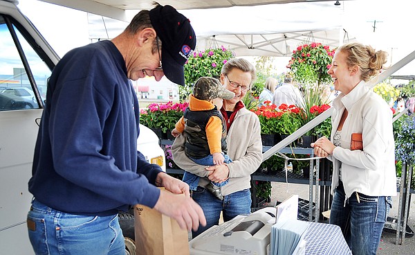 Janette Braaten, center, shares a laugh with customer Courtney Townley of Kalispell and her son Liam, 7 months, as Duane prepares an order on Saturday morning at the Farm-To-Market Pork stand at the Farmer's Market.