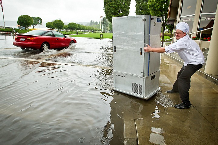 <p>JEROME A. POLLOS/Press John Farmer, a kitchen supervisor at The Coeur d'Alene Resort, struggles to pull a cart of food up onto a flooded sidewalk along Front Avenue following a heavy rain storm Friday. The storm water system was quickly brought overcapacity as the downpour surged through drains and gutters.</p>