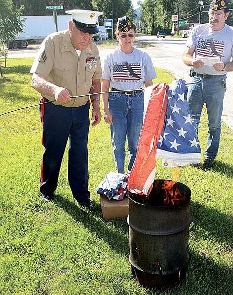 Photo by Nick Ianniello John Cochran (left) lowers an old tattered flag into the flames as Ellen Matz watches and Ernie Ornelas reads a prayer. The St. Regis American Legion puts on a flag retiring ceremony at Mullan Square in St. Regis every year to discard of worn out flags.