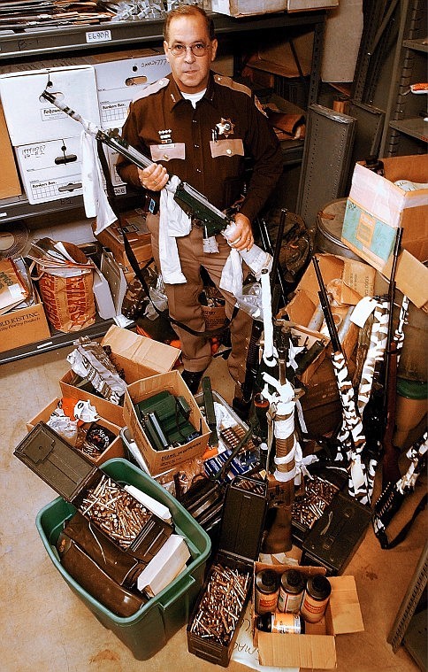 Jim Dupont, then Flathead County sheriff, displays some of the weapons and approximately 25,000 rounds of ammunition being held as evidence in the David Burgert case in February 2002. Dupont holds the fully automatic machine gun Burgert was carrying during an all-night standoff with law enforcement.