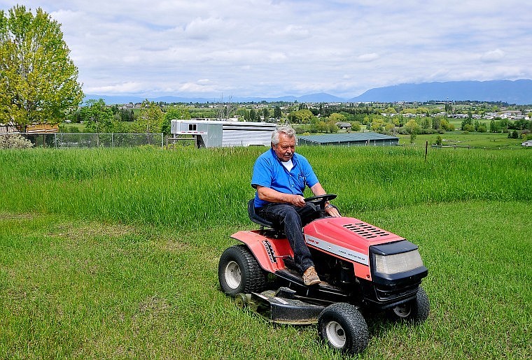 Ron Burow mows the lawn Tuesday afternoon on his property that overlooks part of the Flathead Valley off of U.S. 2 West. The valley has received 4 inches of rain so far this month, causing grass to grow plenty deep in places.