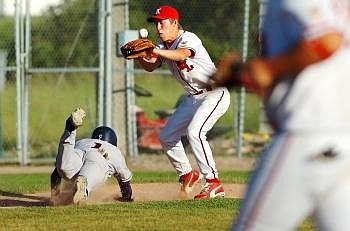 Caught in a pickle between third base and home, Great Falls Electrics player Ethan Hortick dives back to third base as a ball thrown by Kalispell Lakers catcher Greg Seaman floats over Lakers' third baseman Mat O'Brien's glove before hitting him in the nose, causing a short delay during the nightcap of a conference doubleheader Tuesday evening. Nate Chute photo/Daily Inter Lake