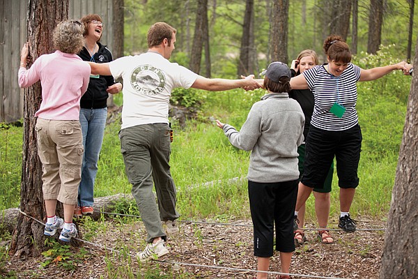 <p>For One Another Family Camp participants and volunteers help each other along the tightrope obstacle on June 22 in Kalispell.</p>