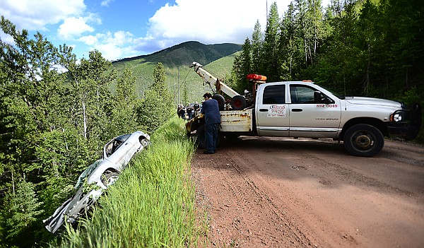 <p>A tow truck driver from American Towing works to pull a car up from where it landed after sliding off the North Fork road and flipping on its way down on Saturday afternoon, June 22, just north of the entrance into Glacier National Park. The driver was not seriously injured. (Brenda Ahearn/Daily Inter Lake)</p>