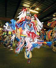 Louie Plant Sr. flashes brightly colored ribbons and feathers as he spins under the lights during the grand entry at the Arlee Powwow Saturday night.