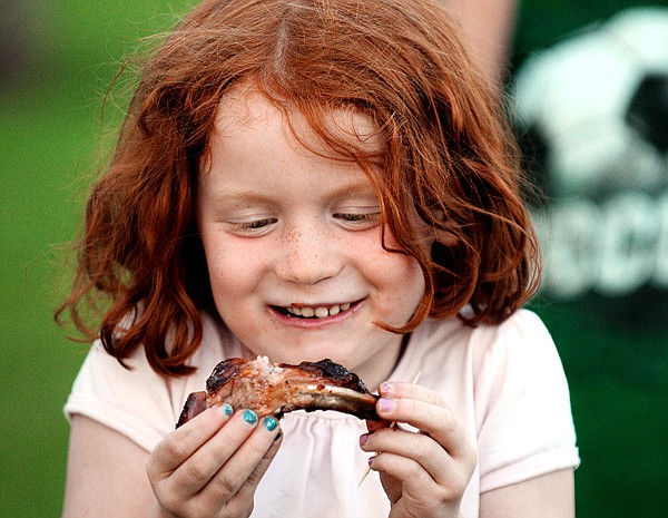Alli Kernana, 6, of Kalispell, enjoys some barbeque ribs prepared by Greg Dulin and David Gassaway on Friday night at the park in Stillwater Estates. Dulin and Gassaway, the &quot;Smokin' Hot Grill Friends&quot; cooked all night preparing for the park dedication on Saturday afternoon.