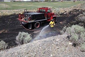 A Moses Lake firefighter extinguishes a brush fire Monday. Juveniles are believed to have started the fire and high winds fanned it out of control.