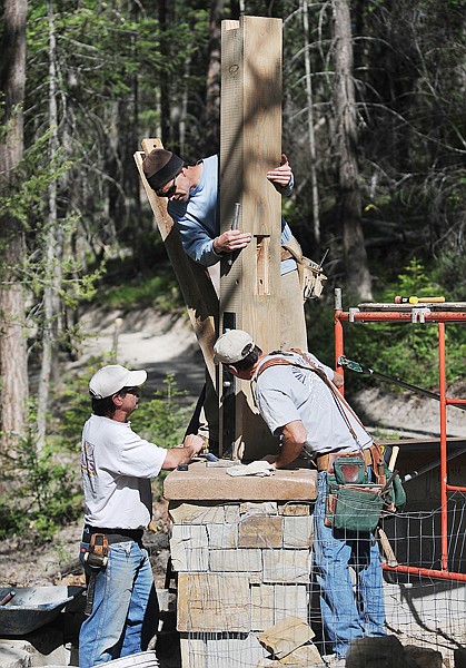 Steve French of Columbia Falls, left, Ken Ellis of Kalispell, top center, and Mike Koness of Kalispell, all of Centennial Timber Frames, installing the new sign that marks the start of the Whitefish Trail on Tuesday morning.