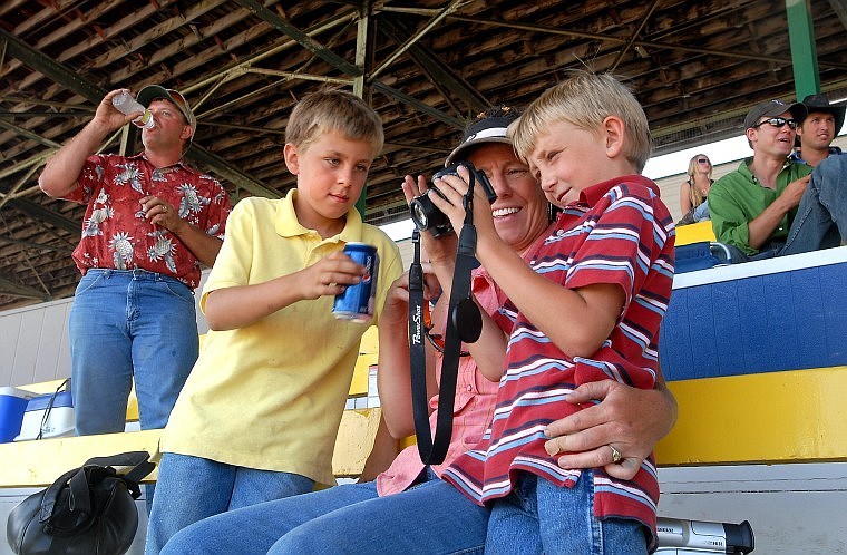 Cameron Kohr, 7, shows his mom Tonya, and older brother Cooper, 9, images from O-Mok-See races while dad Shawn, left, takes a swig of a water in the grandstand at the Flathead County Fairgrounds on Wednesday afternoon.