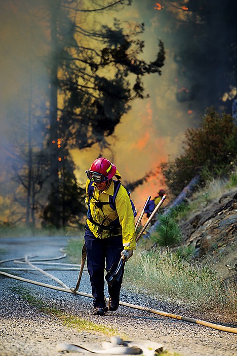 &lt;p&gt;A firefighter hauls a section of hose up the road where the Mica Bay fire burns in the background.&lt;/p&gt;