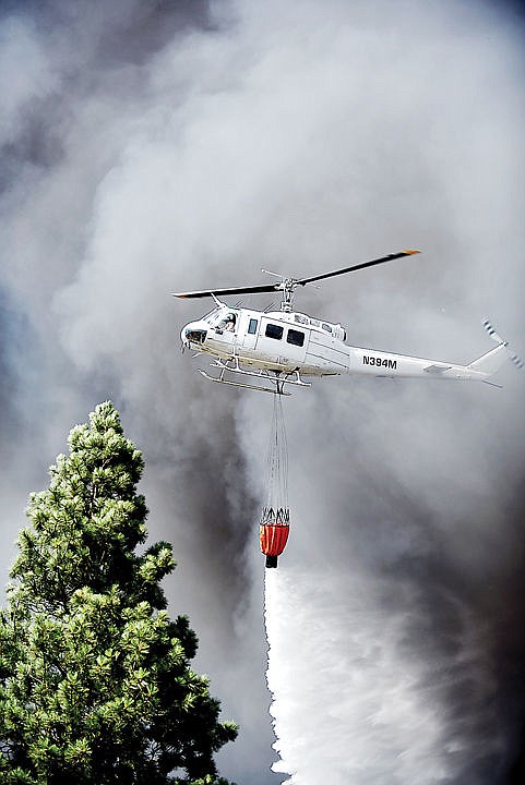<p>A DNRC helicopter flies through smoke to drop water on the scene of a massive fire on Mountain View Drive in Evergreen on Wednesday, August 5. Evergreen Fire and Rescue were joined by the Kalispell and Creston fire departments, the Flathead County Sheriff's Office, forest firefighters and other first responders. (Brenda Ahearn/Daily Inter Lake)</p>