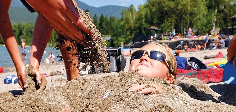 Paige Lowen grimaces while family and friends bury her in the hot sand at Whitefish City Beach.