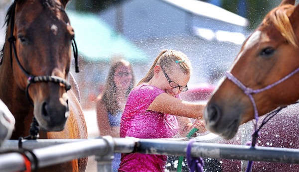 Lilly Diegel, 15, of Kalispell shrieks as she gets a blast of water from Andora Tutvedt, 17, of Kalispell, not shown, as they was wash their horses on Friday at the Flathead County Fairgrounds. In the background is Lilly's sister Eliza Diegel, 14.