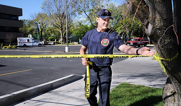 Taylor Zachary of the Kalispell Fire Department removes the caution tape which surrounded the parking lot of the Earl Bennett Building on Friday morning.