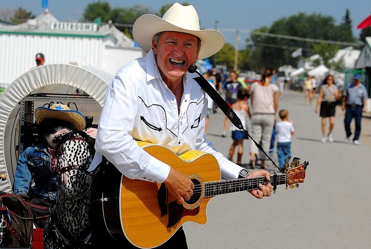 With the sounds of country classics coming from a sound system in the covered wagon, Bruce Mullen performs for passing fairgoers on Wednesday afternoon as part of his musical act, Travl&#146;n Opry.