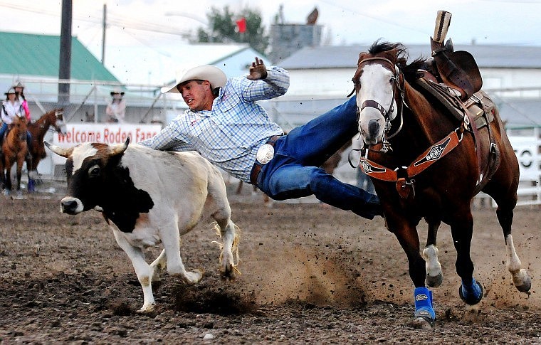 Trevor Knowles of Mount Vernon, Ore., slides off of his horse to wrestle a steer Saturday night during the final performance of the Northwest Montana Fair PRCA Rodeo.