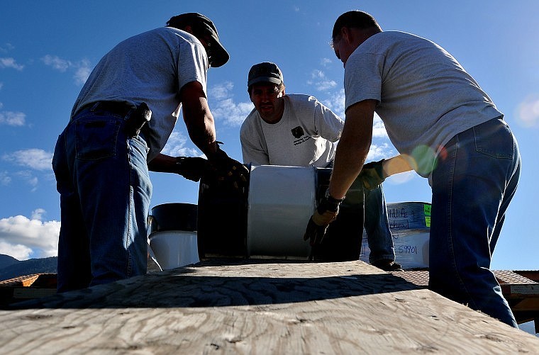 From left, Gary Michael, Grant Grisak, and Mark Schnee begin to roll one of the barrels carrying rotenone to the ground. Each barrel weighed about 285 lbs.