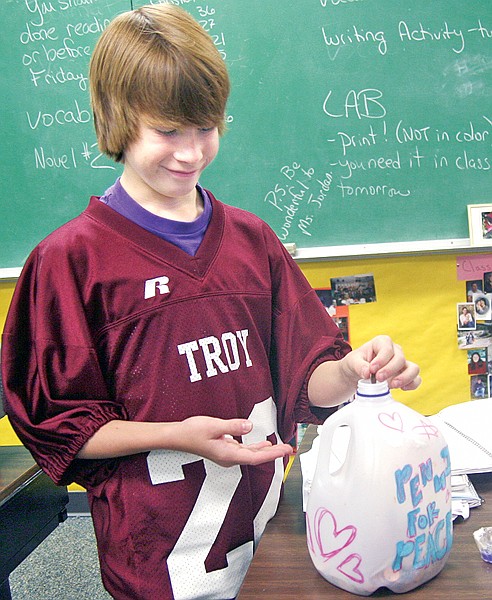 Troy eighth-grader Ty Hight places change in a milk jug. At the time, the eighth-grade girls were beating out the boys in the amount of money raised for Pennies for Peace.