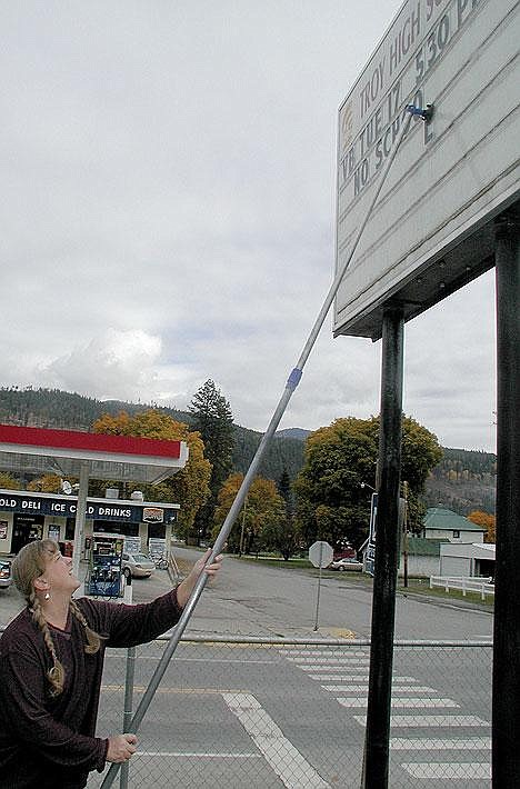 Kay Randall uses a 12-foot pole to changed the message on Troy Public Schools' 15-foot high announcement board. Troy plans to replace the board outside the high school with an electronic reader board.