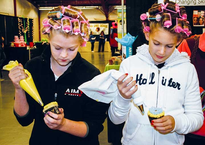 Hanna Nelson and Maddie Higgins, both of Moses Lake, decorate cupcakes at the Michael's booth at the Columbia Basin Women's Expo Saturday. (The curlers were part of their preparation for some Halloween pictures, they said.)