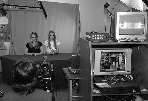 Pirates New Network eight grade reporters Dallas Burris, left, and Anna DiGiallonardo, right, practice their opening lines in front of a green screen while eighth grader Jonel Kallowat, front, runs the camera. The two reporters are shown on the monitor at right with a digital background.
Photo by Mike Cast