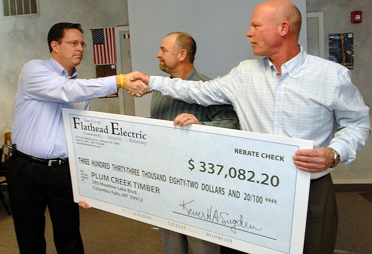 Mark Johnson, left, Flathead Electric Cooperative assistant general manager, shakes hands with Ken Benson, Plum Creek electrical engineer, while Bob Hickey, product-line manager for Plum Creek Medium Density Fiberboard, holds a rebate check given to the company Thursday morning.