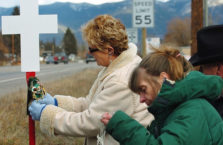 Darla Weller, left, attaches a memento to her daughter Marica&#146;s white cross on Montana 35. On the right are Rita Leeseberg and Gary Weller. Marica Weller died when she was struck by a vehicle while she was walking across the highway on Oct. 15. Darla Weller said she hopes the street light at the intersection of Montana 35 and Shady Lane would flash red instead of yellow all night long to keep drivers aware of pedestrians in the area.