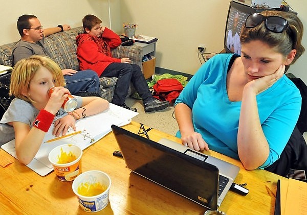 Cinda works on some homework related to her degree in human services while Alena takes a drink of orange soda and the boys watch a news broadcast.