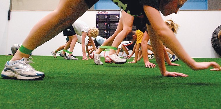 Participants in the class do a bear crawl with elastic ankle bands wrapped around their legs across the Astroturf surface.