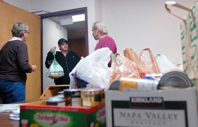 Roger Basso holds up a bag of canned goods Friday afternoon to hand off to Luke Chapman and Mary Vollertsen at Kalispell Municipal Court as part of the court&#146;s Food for Fines program.